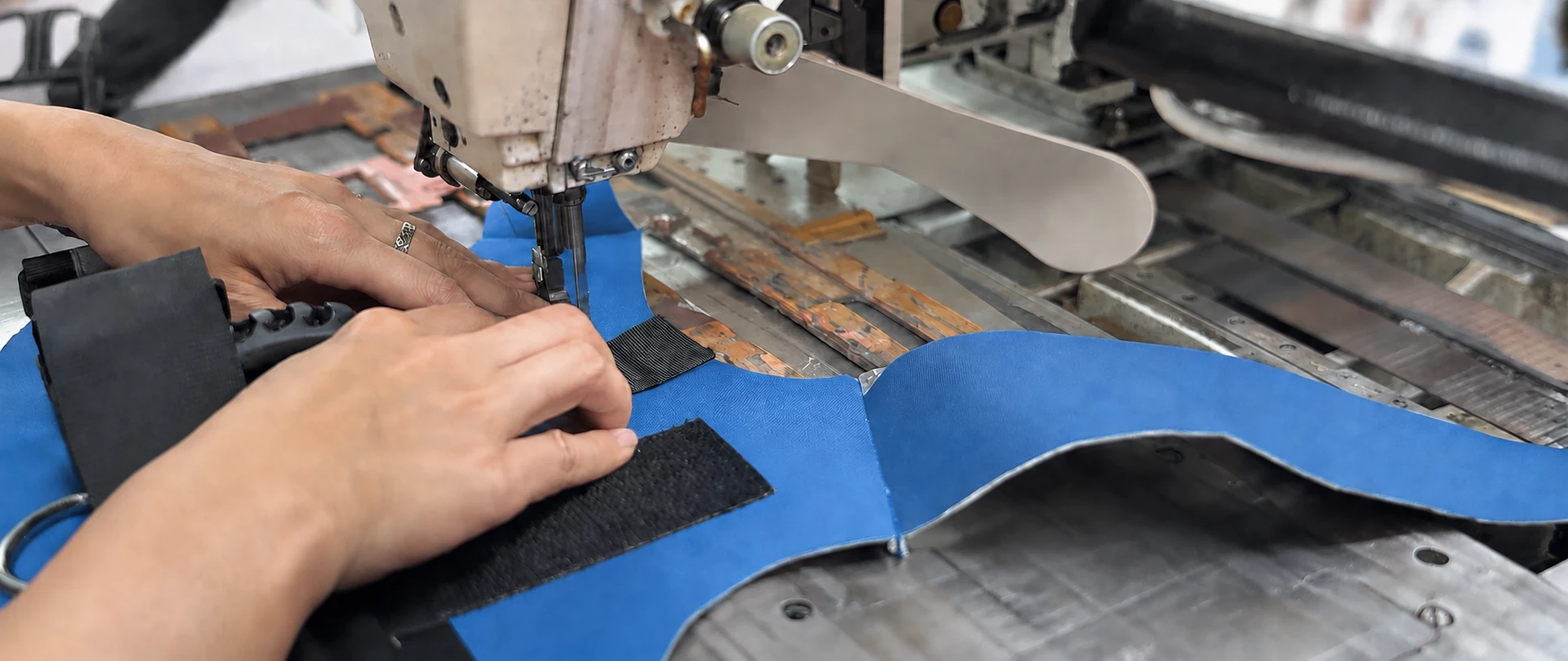 Hands guiding a blue pet harness panel under a sewing machine